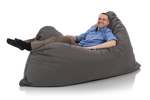 Junger Mann liegt gemuetlich in einem riesigen Kissen anthrazit der Groeße 120 x 180 cm